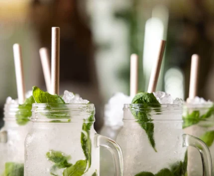 Refreshing mint mojitos in mason jars with straws, set in a vibrant, social atmosphere.