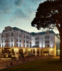 Elegant hotel exterior with warm lighting at dusk, surrounded by lush greenery and inviting ambience.