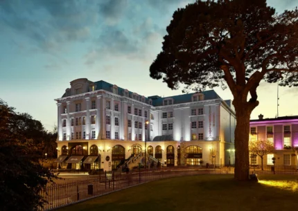 Elegant hotel exterior with warm lighting at dusk, surrounded by lush greenery and inviting ambience.
