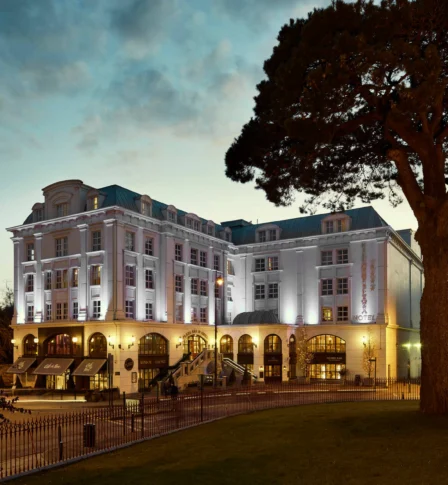 Elegant hotel exterior with warm lighting at dusk, surrounded by lush greenery and inviting ambience.