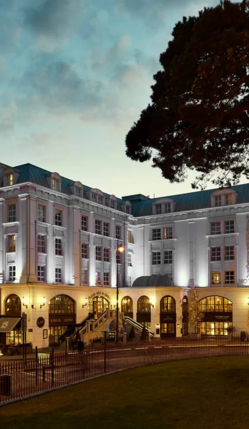 Elegant hotel exterior with warm lighting at dusk, surrounded by lush greenery and inviting ambience.