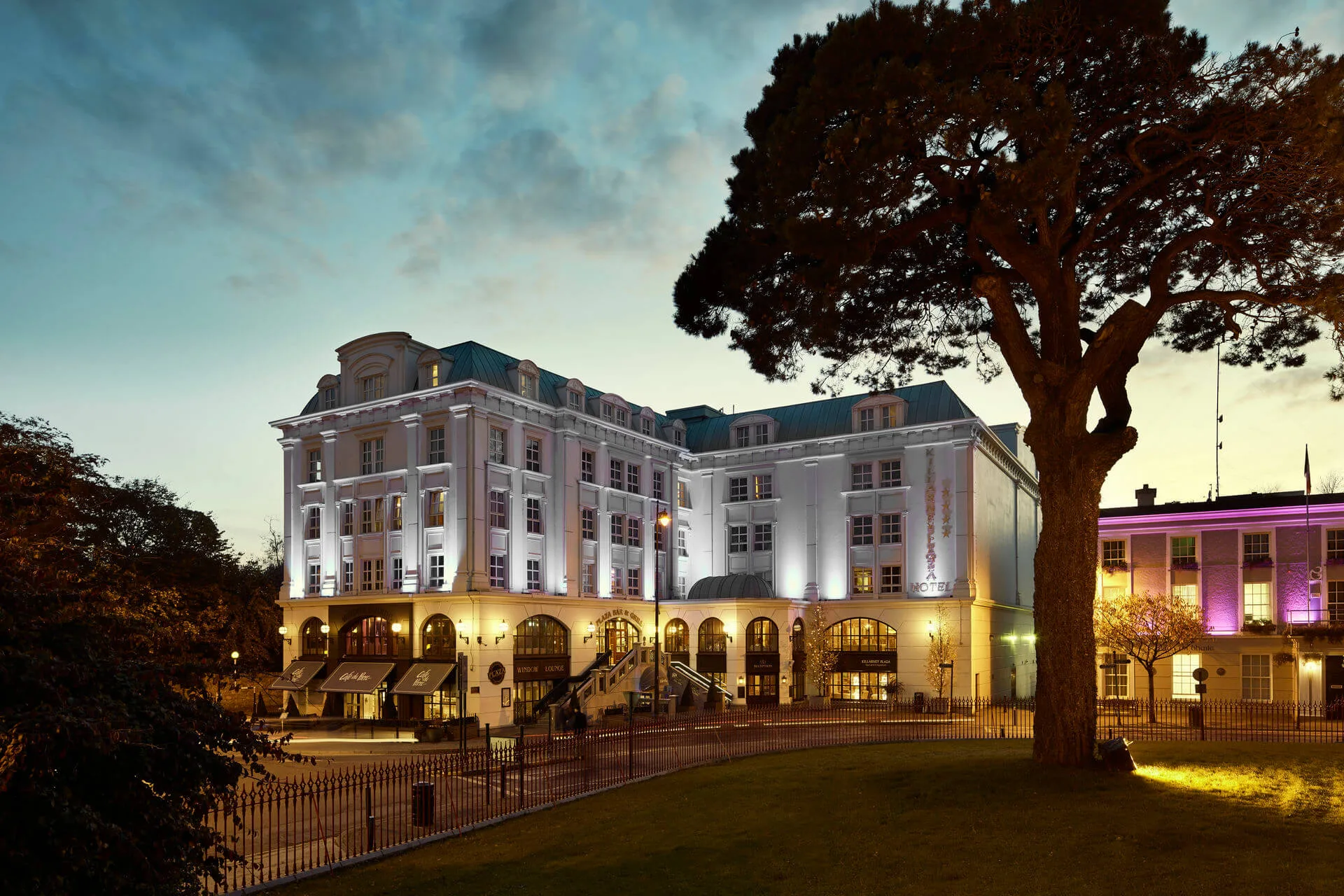 Elegant hotel exterior with warm lighting at dusk, surrounded by lush greenery and inviting ambience.