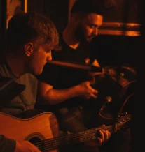 A warm, cosy setting with two musicians playing traditional music.
