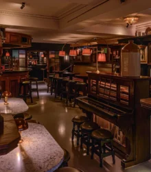 Cosy pub interior with wooden decor and dim lighting, featuring tables and a piano.