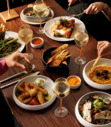 A group of people enjoying a meal with diverse dishes and wine at a cosy restaurant.