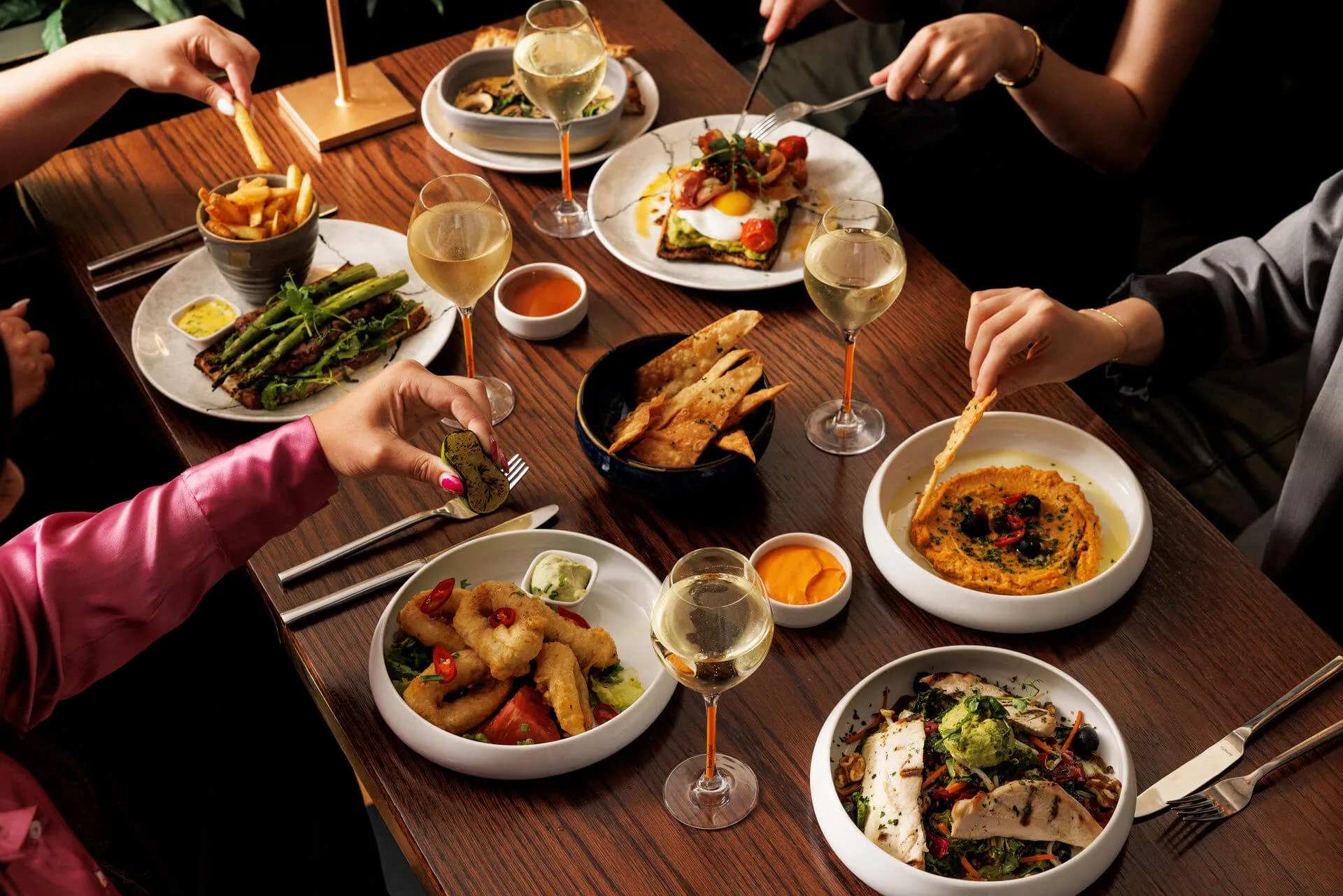 A group of people enjoying a meal with diverse dishes and wine at a cosy restaurant.