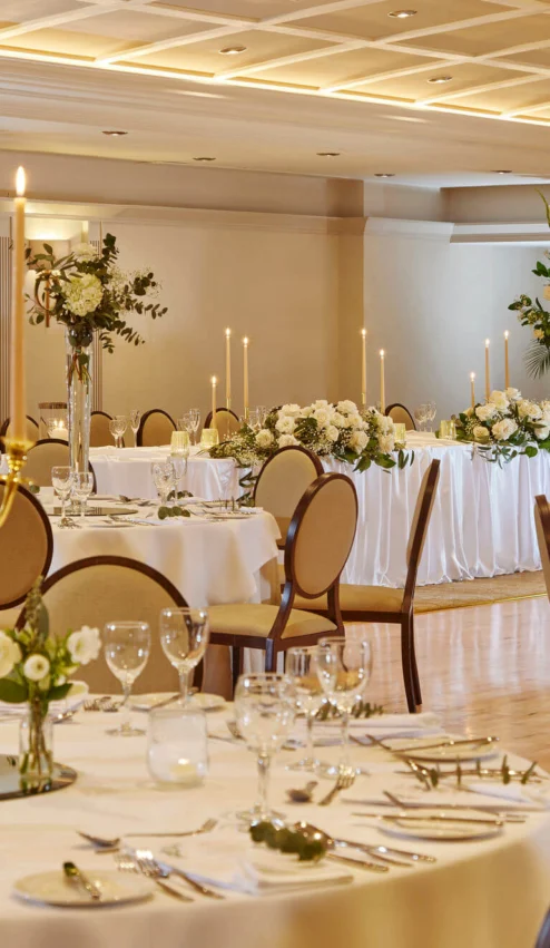 Elegant banquet hall with beautifully set tables, adorned with floral centrepieces and candles.
