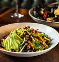Delicious salad with avocado and a glass of wine in a cosy restaurant setting.