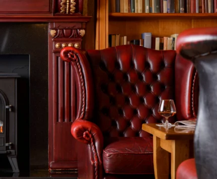 Cosy hotel lounge with red leather chairs and a fireplace.