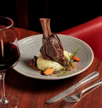 Elegant lamb shank dish with wine in a warm, upscale restaurant setting.