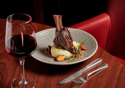 Elegant lamb shank dish with wine in a warm, upscale restaurant setting.