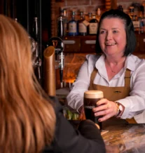 Bartender serves pint of Guinness to guest in cosy pub setting.