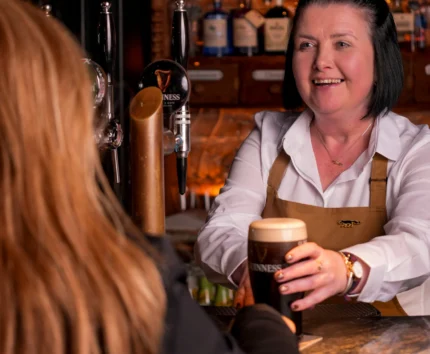 Bartender serves pint of Guinness to guest in cosy pub setting.