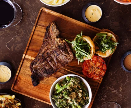 Family enjoying steak dinner with sides in cosy restaurant setting.