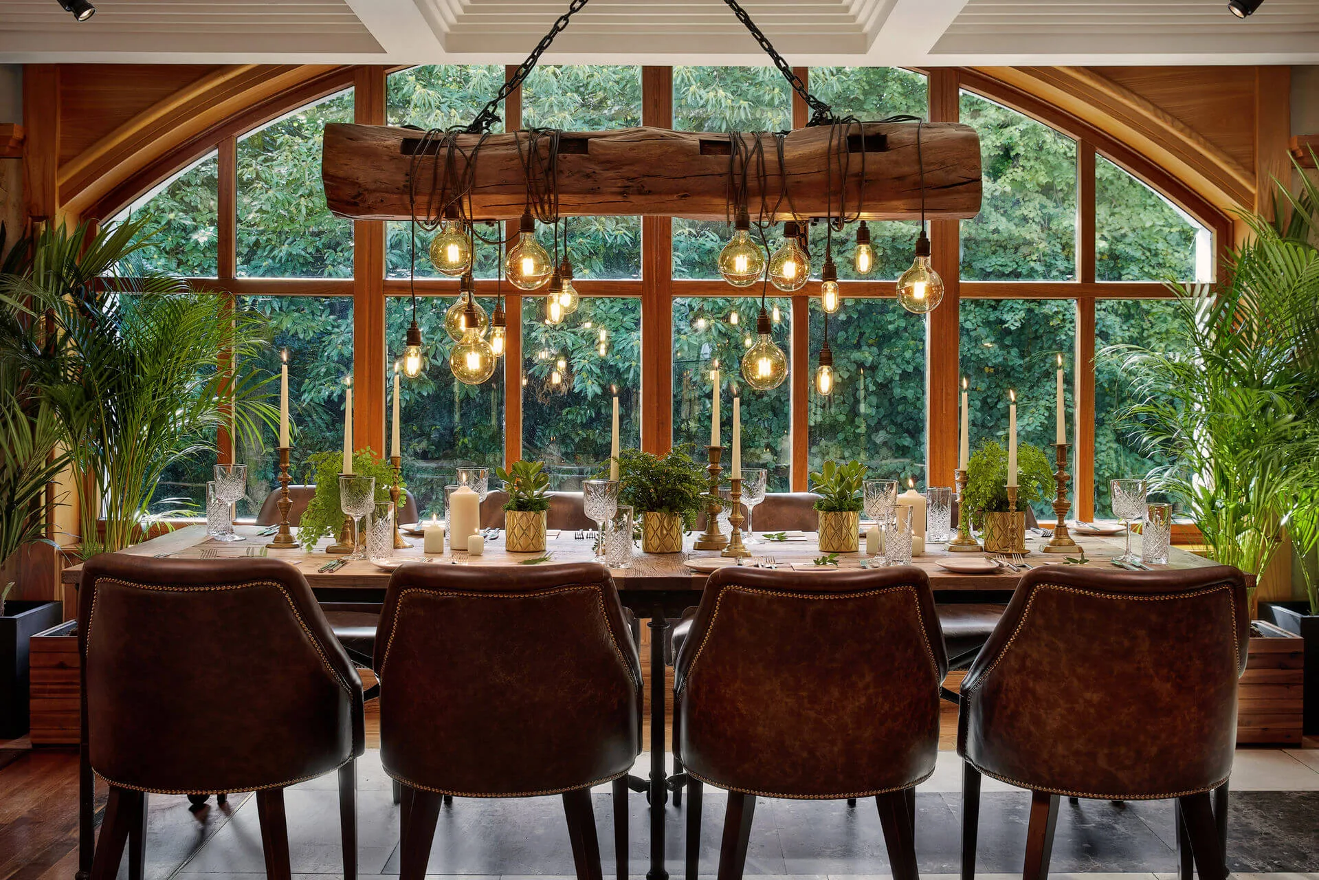 Cosy dining area set with elegant tableware, glowing lights, large window view of greenery.