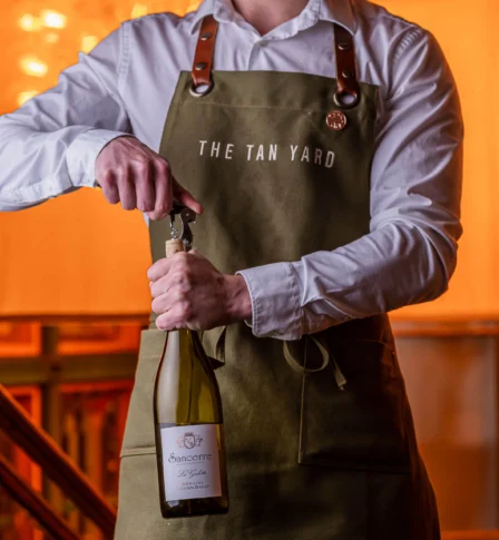 Person opening wine bottle at The Tan Yard restaurant.