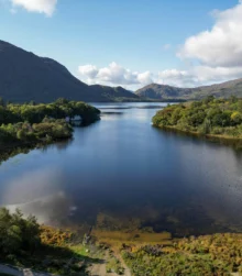Scenic view of a tranquil lake surrounded by lush green hills and mountains under a blue sky.