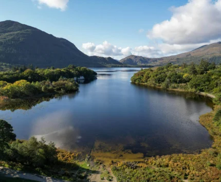 Scenic view of a tranquil lake surrounded by lush green hills and mountains under a blue sky.