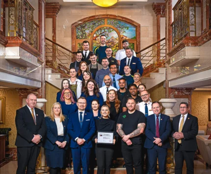 A welcoming hotel team stands on an elegant staircase, holding a framed award.