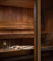 Cosy hotel sauna with wooden benches and drink on towel.