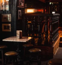 Cosy pub corner with rustic wooden stools and warm lighting.