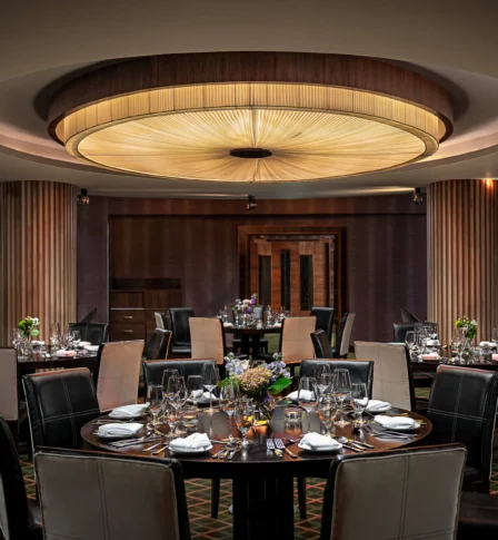 Elegant dining room set for a group, warm lighting, floral centrepieces.