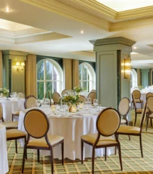 Elegant dining room set for an event with round tables, decorative flowers, and soft lighting.