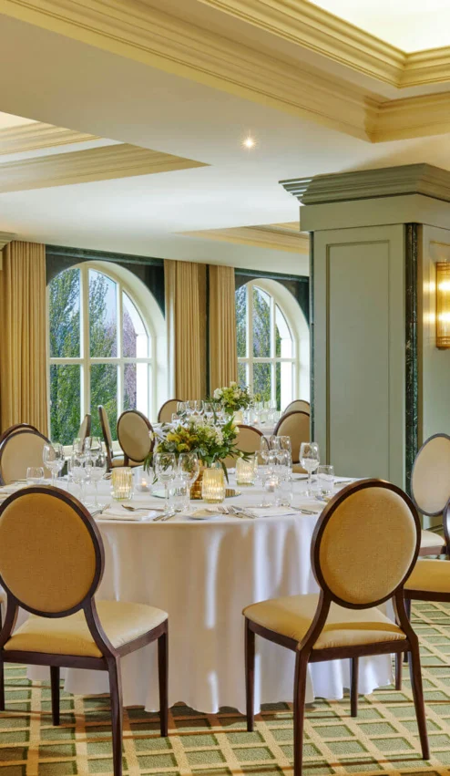 Elegant dining room set for an event with round tables, decorative flowers, and soft lighting.