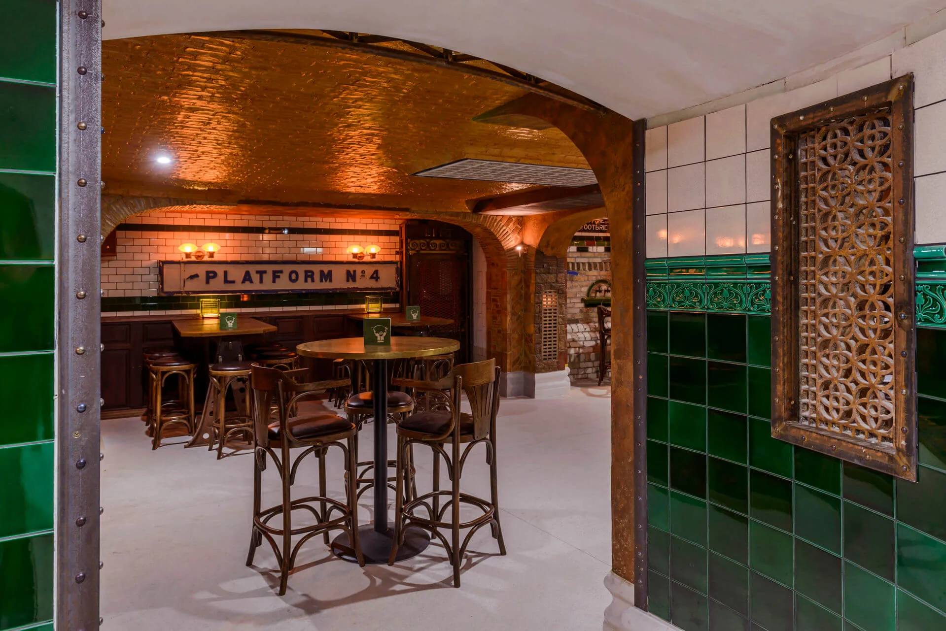 Cosy pub setting with high tables, stools, and ambient lighting, featuring a "Platform No. 4" sign.