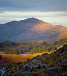 Scenic view of a sunlit mountain and lush valley, inviting natural beauty.