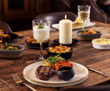 Cosy dining table with steak, sides, candle, and drinks.