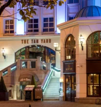 Entrance to a warmly lit hotel with "The Tan Yard" sign, elegant exterior stairs.