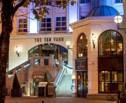 Entrance to a warmly lit hotel with "The Tan Yard" sign, elegant exterior stairs.