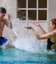 A joyful couple splashing water in an indoor hotel pool.