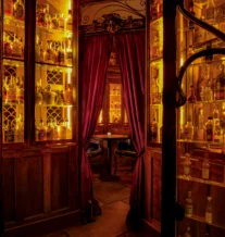 Cosy, dimly-lit bar alcove with rich wood cabinets and glowing amber bottles.