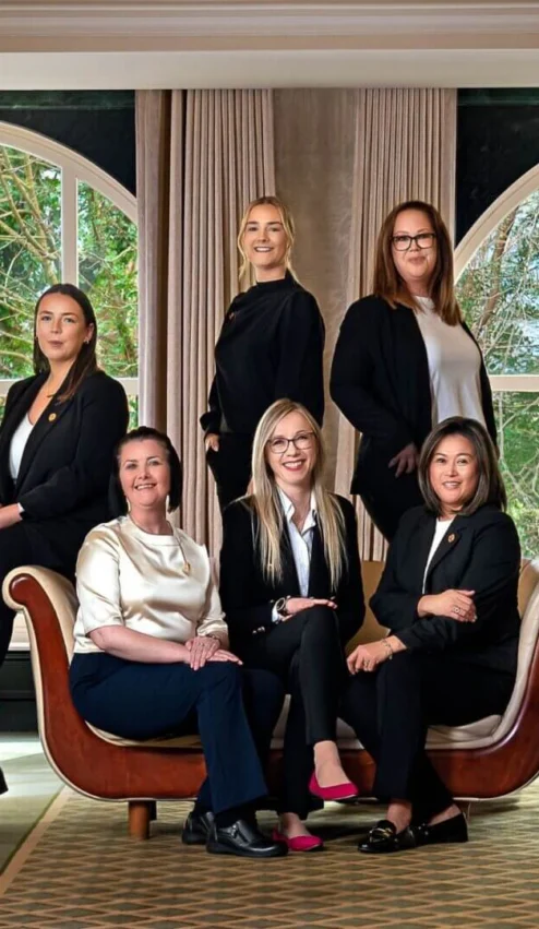 A warm and welcoming hotel team posing together in a spacious, elegantly furnished lounge.
