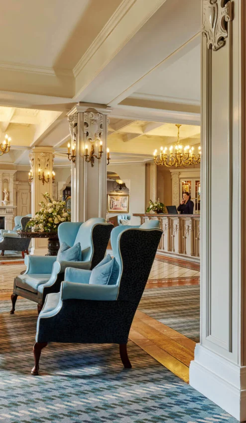Elegant hotel lobby with cosy seating and chandeliers, welcoming guests at reception.