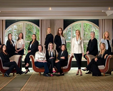 A welcoming hotel team of women and a couple gathered in a bright lounge, chatting and smiling