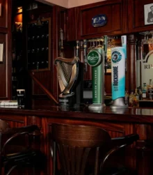 Cosy hotel bar with wooden decor and seating, showcasing vintage photos and a variety of drinks.