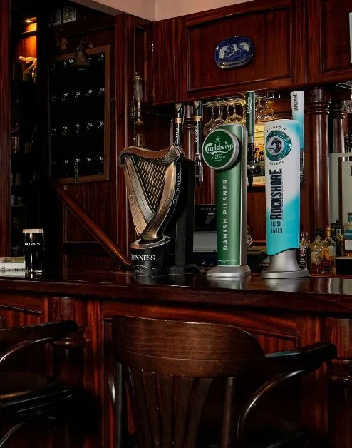 Cosy hotel bar with wooden decor and seating, showcasing vintage photos and a variety of drinks.