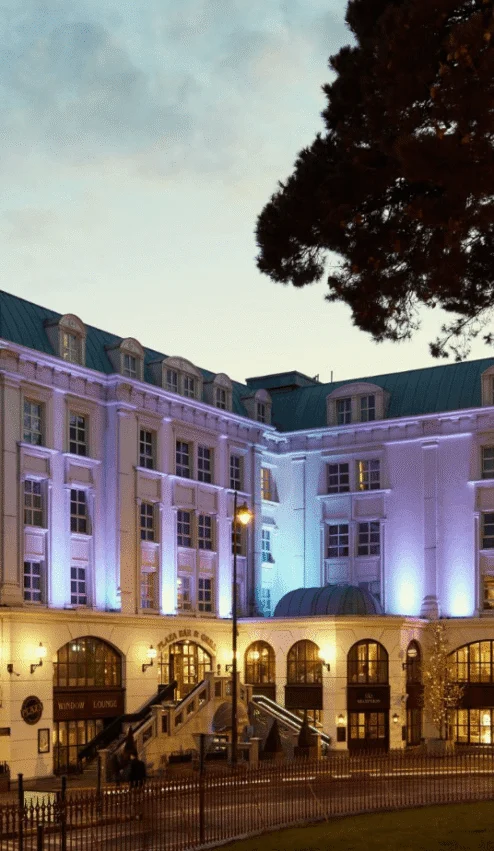 Grand hotel exterior with warm lights and tree in evening setting.