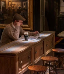 Man enjoying a pint of Guinness while reading at a cosy pub bar.