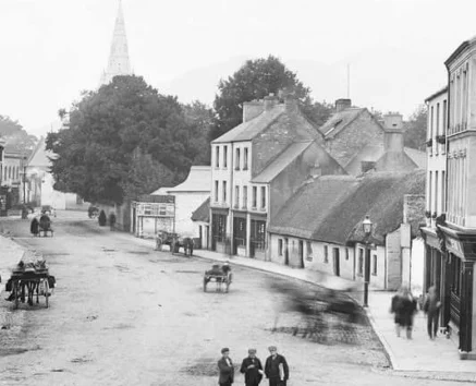 Family strolling along a historic town street with shops, horse carts and church spire visible