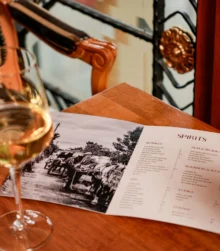 Wine glass on table with open spirits menu in cosy, warmly lit room.