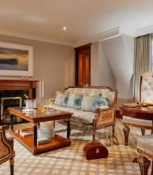 Elegant hotel suite with plush seating, a table set for two, and ambient lighting.