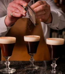 Skilled bartender gratefully garnishing three Irish coffees in a welcoming atmosphere.