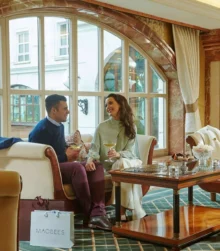 A couple enjoying tea in a cosy hotel lounge with large windows.