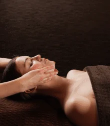 Relaxed guest receiving a soothing facial massage on a brown spa couch, warm ambient setting