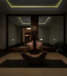 Woman practising seated yoga on a mat in a calm hotel wellness studio with warm lighting and mirror