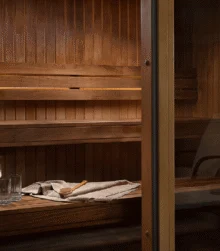 Family enjoying a warm wooden sauna with towels, a water jug and glasses on the bench